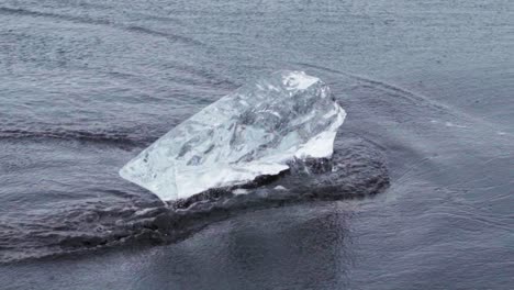 Gentle-water-flowing-around-chunks-of-ice-on-a-black-sand-beach-in-Iceland---Slow-motion