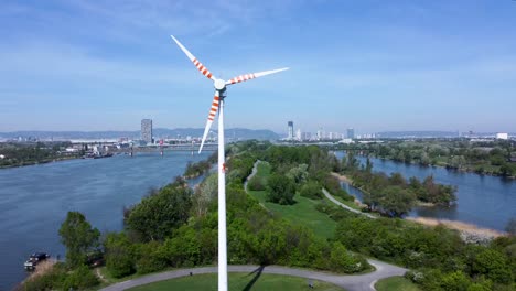 Aerial-shot-of-a-wind-turbine-on-Danube-Island-with-Vienna-skyline-in-the-background,-sunny-day