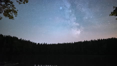 Calm-forest-lake-at-night-with-clouds-and-the-starry-night-milky-way,-tilt-up