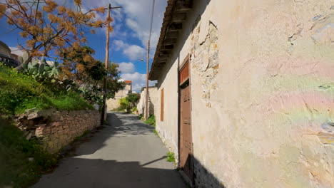 Eine-Sonnendurchflutete-Gasse-In-Lefkara,-Gesäumt-Von-Traditionellen-Weißgetünchten-Wänden,-Einer-Alten-Holztür-Und-Einem-Blühenden-Baum,-Die-Den-Rustikalen-Charme-Des-Dorfes-Widerspiegeln