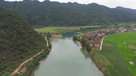 Aerial-Drone-Shot-of-River-Passing-Through-Mountain-Range-with-Grass-Fields-in-Vietnam