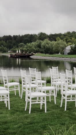 Weiße-Leere-Holzstühle-Stehen-Auf-Grünem-Rasen-In-Der-Nähe-Des-Sees