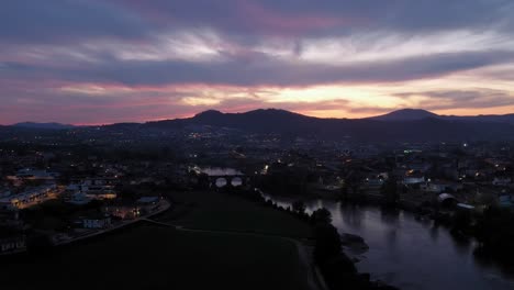 Twilight-hues-over-Barcelos,-with-the-medieval-bridge-spanning-the-serene-river,-Portugal---aerial