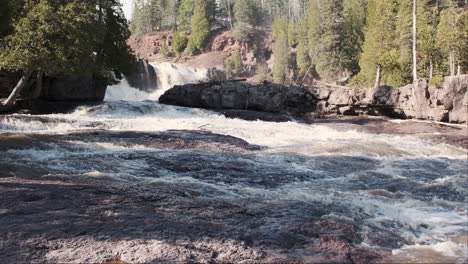 Gooseberry-Falls-cascades-over-a-rugged-rocky-riverbed,-surrounded-by-lush-greenery