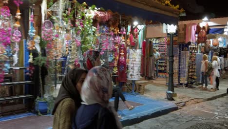 Traditionelle-Arabische-Frauen-Gehen-Nachts-Vor-Den-Lebhaften-Und-Beleuchteten-Souvenirläden-Im-Zentrum-Von-Chefchaouen-In-Marokko