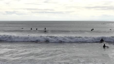 Surfers-paddle-and-push-through-incoming-waves---Scarborough-Bay,-Christchurch,-New-Zealand