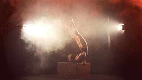 Female-contortionist-in-dramatic-smoky-scene-does-chest-stand-on-box