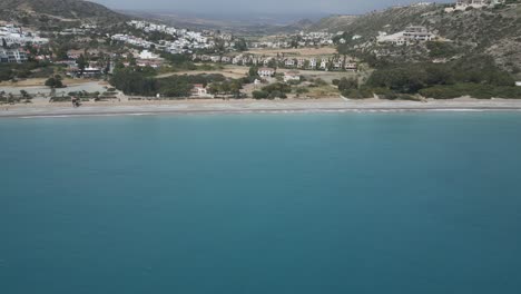 Playa-De-Pissouri-En-Chipre,-Con-Aguas-Cristalinas-De-Color-Turquesa-Y-Telón-De-Fondo-De-La-Ciudad-Costera,-Vista-Aérea