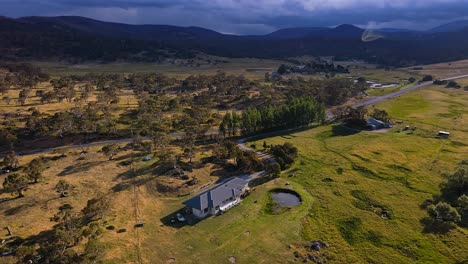 Toma-Aérea-Inclinada-De-Una-Casa-Rural,-Camino-Rural-Y-Nubes-De-Tormenta-En-Crackenback,-Nueva-Gales-Del-Sur,-Australia