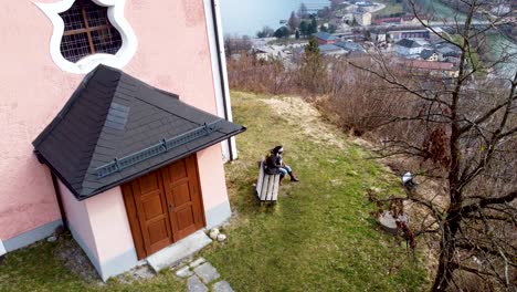 Una-Mujer-Negra-Está-Sentada-Cerca-De-La-Pintoresca-Capilla-De-Kalvarienberg-Con-Vistas-A-Traunsee-En-Ebensee,-Alta-Austria,-Enmarcada-Por-Los-Alpes