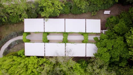 drone-aerial-view-of-a-white-garden-walkway-with-green-plant-arches,-large-white-fabric-panels-to-protect-from-rain-or-sun,-ideal-for-a-wedding-ceremony