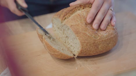 Hands-cutting-fresh-loaf-of-bread,-close-up