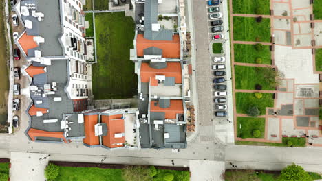 Directly-overhead-aerial-view-of-a-row-of-terracotta-roofed-buildings-in-Elbląg,-bordered-by-a-street-with-parked-cars-and-a-green-grassy-area