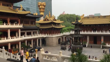 Courtyard-of-Jingan-Temple-in-Shanghai,-China-with-tourists,-skyscrapers-in-background