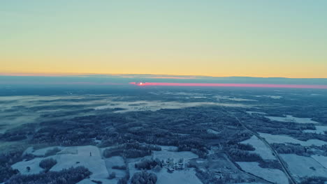 Aerial-winter-sunrise-over-a-tranquil-snowy-landscape,-hint-of-pink-on-horizon