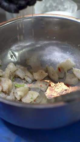 Throwing-lemon-juice-to-ceviche-in-metal-bowl,-black-gloved-chef,-vertical-close-up