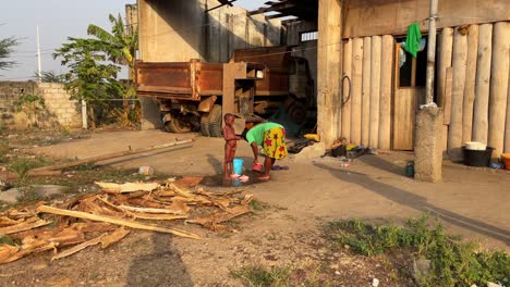 Madre-Negra-Africana-Se-Ducha-Con-Un-Balde-Para-Ahorrar-Agua-A-Su-Pequeño-Y-Lindo-Hijo-En-Una-Pobre-Y-Remota-Aldea-Rural-De-África