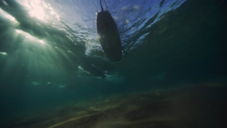 Underwater-view-below-crowd-of-longboarders-surfing-on-sandy-beach-at-sunrise