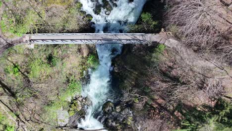 Aerial-view-of-a-pedestrian-bridge-over-the-rushing-waters-at-Seerenbachfälle,-Walensee's-hidden-gem