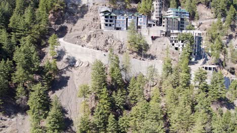 Aerial-view-of-multi-level-buildings-constructed-along-a-winding-mountain-road,-surrounded-by-pine-trees