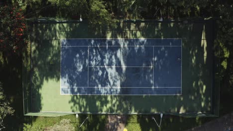 Tennis-players-challenge,-sports-court-venue,-nature-all-around,-aerial