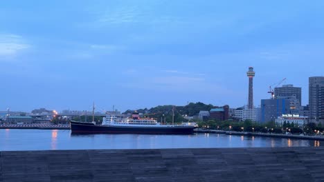 Die-Morgendämmerung-Bricht-über-Einer-Ruhigen-Uferpromenade-An,-Ein-Großes-Schiff-Liegt-Dort-Vor-Anker-Und-Man-Sieht-Die-Moderne-Skyline