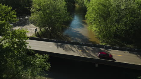 Wolf-river-flowing-under-a-bridge-in-collierville,-tennessee,-surrounded-by-lush-greenery,-aerial-view