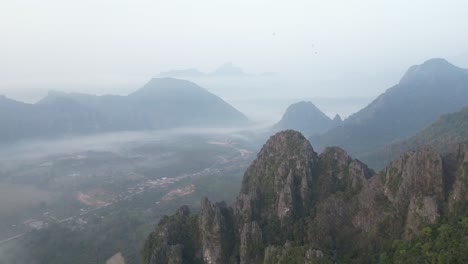 drone-shot-flying-over-cliffs-into-the-valley-in-Vang-Vieng,-the-adventure-capital-of-Laos