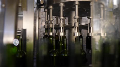 Empty-green-glass-bottles-filling-with-red-wine-at-an-automated-production-line-in-Vignonet-France,-Medium-shot