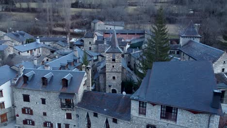 Historic-stone-houses-of-Anciles-nestled-in-the-Aragonese-Pyrenees,-with-Spain-snow-capped-peaks-in-the-background---Aerial