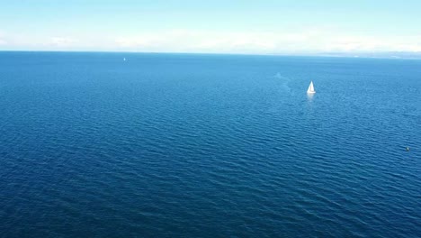 Aerial-push-from-shore-to-sea-with-sailboat-in-background-on-blue-sea