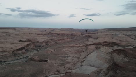 In-Den-Weiten-Himmeln-Von-Utah,-USA,-Manövriert-Ein-Einsamer-Gleitschirm-Anmutig-Und-Gleitet-Friedlich-über-Das-Zerklüftete-Und-Trockene-Gelände-Und-Verkörpert-Freiheit-Inmitten-Der-Ausgedehnten-Wüstenlandschaft