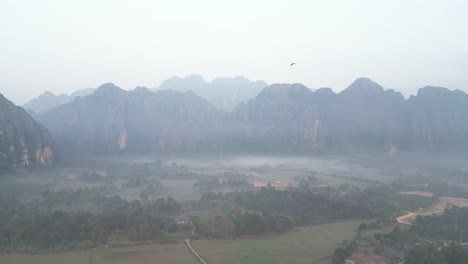 drone-shot-of-foggy-morning-in-the-valley-in-Vang-Vieng,-the-adventure-capital-of-Laos