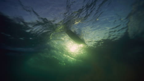 Strong-ocean-waves-break-as-surfers-cross-paths,-view-from-underwater