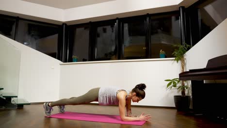 Mujer-Haciendo-Ejercicio-De-Plancha-Sobre-Colchoneta-En-Casa,-Entrenamiento-Nocturno-En-Interiores,-Enfoque-En-La-Salud