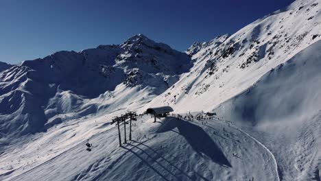 Chair-lift-station-high-in-Alps-during-winter-sport-season,-aerial