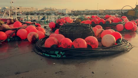 Boyas-De-Color-Rojo-Vivo-Adornan-Los-Muelles-De-Un-Pintoresco-Pueblo-Pesquero-Español,-Firmemente-Sujetas-Al-Muelle-Costero,-Ofreciendo-Una-Visión-Del-Encanto-De-Este-Acogedor-Puerto-Y-Su-Comunidad-Pesquera.