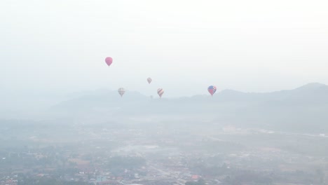Toma-De-Drones-De-Globos-Aerostáticos-Elevándose-Por-Encima-De-La-Niebla-De-La-Mañana-En-Vang-Vieng,-La-Capital-De-Aventuras-De-Laos.