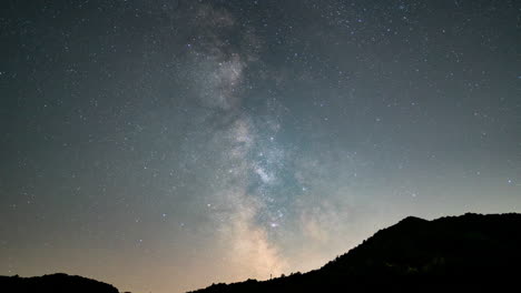 Milky-Way-galaxy-rising-over-a-silhouetted-mountain-peak-at-night,-stars-twinkling,-timelapse