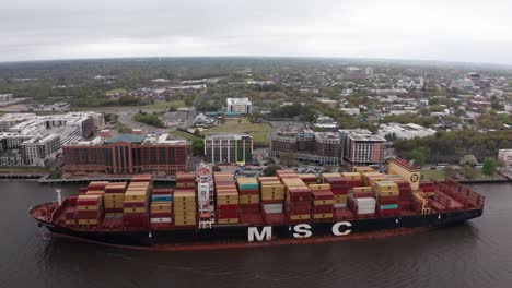 Wide-aerial-dolly-shot-of-an-MSC-cargo-ship-going-down-the-Savannah-River-in-Savannah,-Georgia