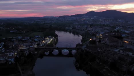 Twilight-over-Barcelos,-with-the-iconic-medieval-bridge-lit-by-streetlights-reflecting-on-the-Cávado-River