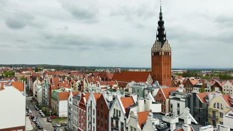 Sweeping-aerial-view-of-Elbląg,-featuring-the-towering-spire-of-the-cathedral-as-it-rises-majestically-above-the-charming-array-of-colorful,-gabled-rooftops-and-narrow-streets-of-the-old-town---Polish