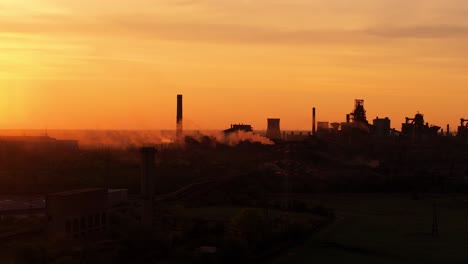 Silhouetten-Von-Industriellen-Schornsteinen-Mit-Rauchemissionen,-Gegen-Die-Lebhaften-Farbtöne-Des-Orangefarbenen-Sonnenlichts,-Hoher-Kontrast