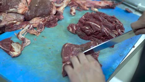 Chef-hands-cuts-raw-meat-with-the-knife-on-a-blue-cutting-board