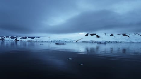 Aerial-Drone-Shot-of-Antarctica-of-Mountains-and-Glacier-with-Dramatic-Blue-Clouds,-Antarctica-Peninsula-Beautiful-Scenery-on-the-Southern-Ocean-Sea-with-Calm-Still-Flat-Water-with-Reflections