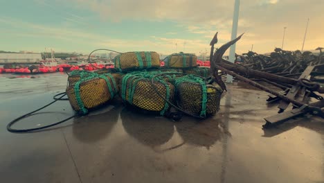 Fishing-gear-rests-on-the-moist-asphalt-in-a-coastal-Spanish-town,-including-metal-anchors-and-nets,-embodying-the-spirit-of-maritime-livelihood-and-coastal-heritage