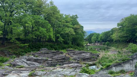 Scenic-outdoor-view-of-rocky-terrain-with-lush-green-trees-and-a-cloudy-sky