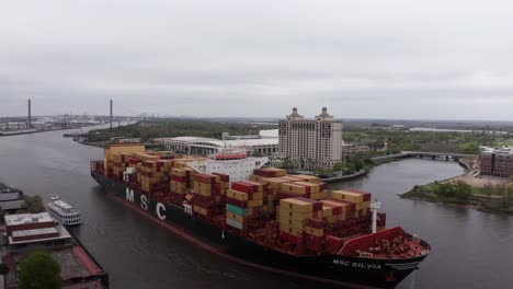 Aerial-wide-reverse-pullback-shot-of-an-MSC-cargo-ship-going-down-the-Savannah-River-in-Savannah,-Georgia