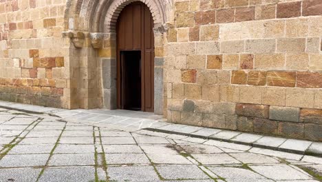 Filmacion-Del-Pórtico-De-La-Iglesia-De-San-Nicolas-En-Avila,-Hay-Un-Piso-De-Losas-De-Granito-Gris-Y-Con-La-Cámara-Elevada-Vemos-La-Puerta-Con-Sus-Hermosos-Detalles-Y-Su-Fachada-España