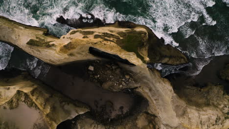 Aerial-top-down-view-rising-above-eroded-sandstone-cliffs-of-Cape-Kiwanda,-Oregon-Coast